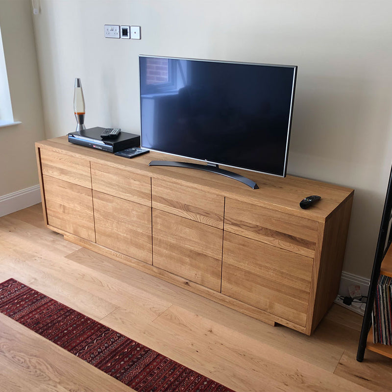 Linn sideboard with flat handle less front. four drawers over four doors- shown with tv on stand sitting on it, 