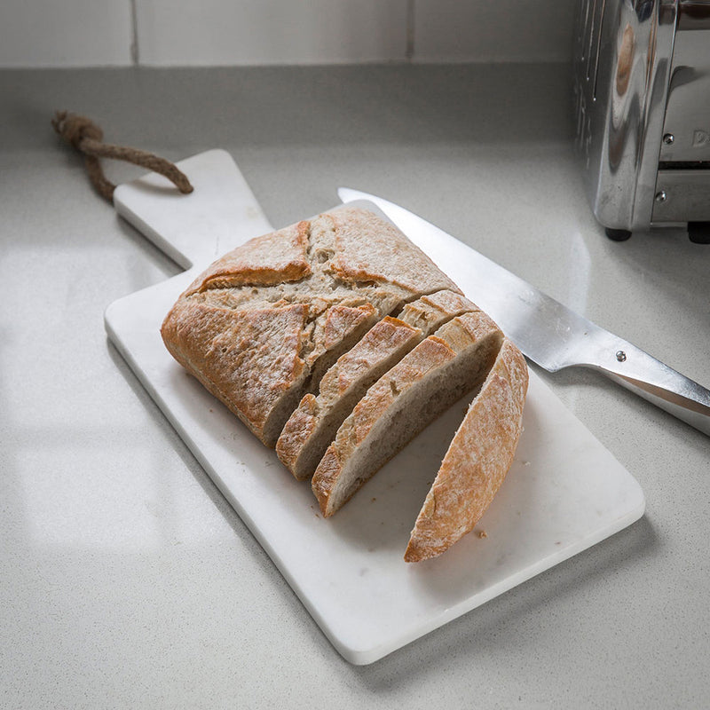 white marble rectangle serving board shown with fresh sliced bread 