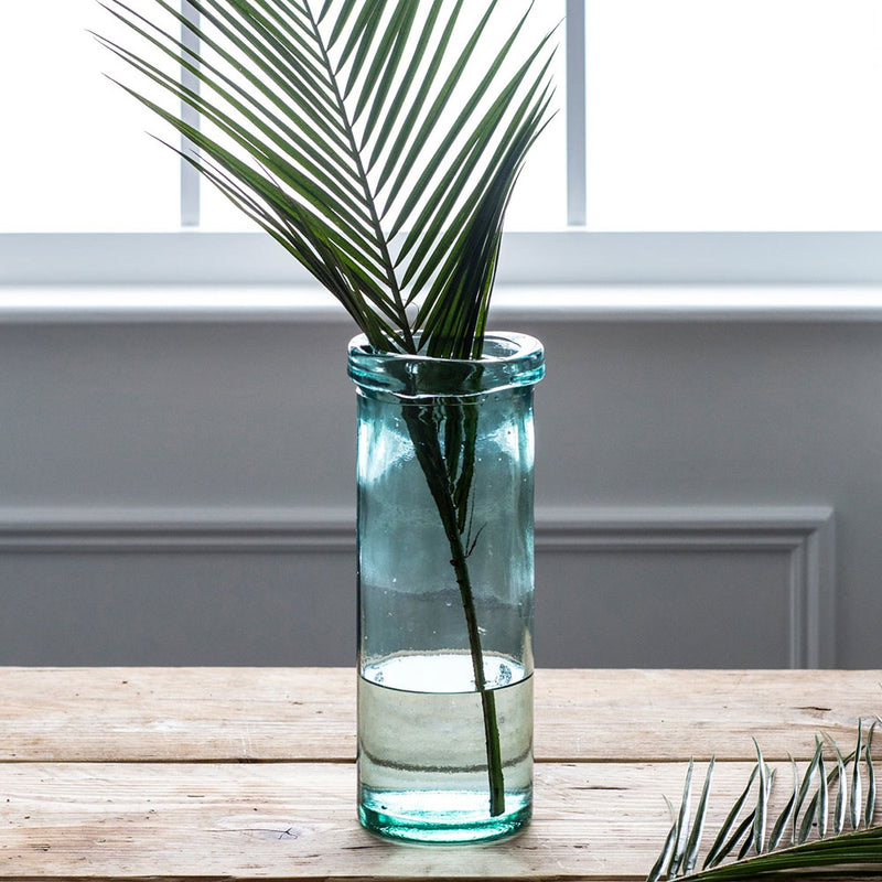 Thick green glass vase on table with fern leaf inside