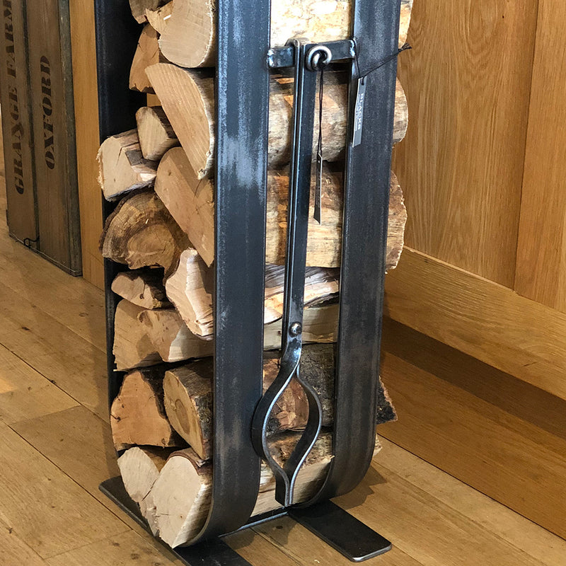 Fire tongs shown hanging on a log holder.