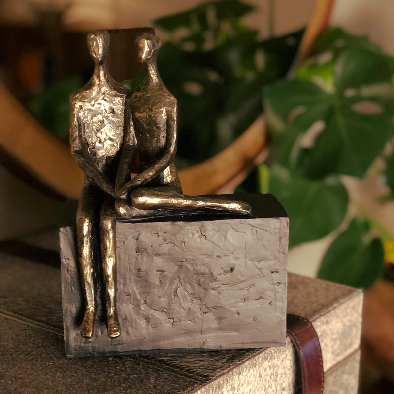 Seated couple sculpture, he is sitting on a large block, she is curled next to him, holding hands