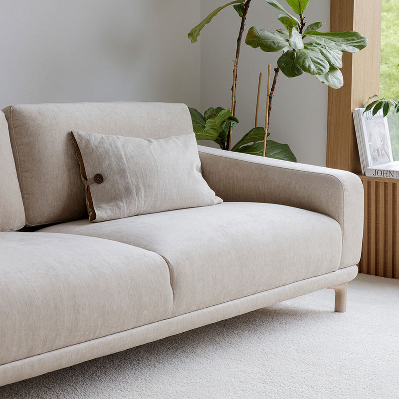 Beige sofa with a pillow in a room with plants and a bookshelf.