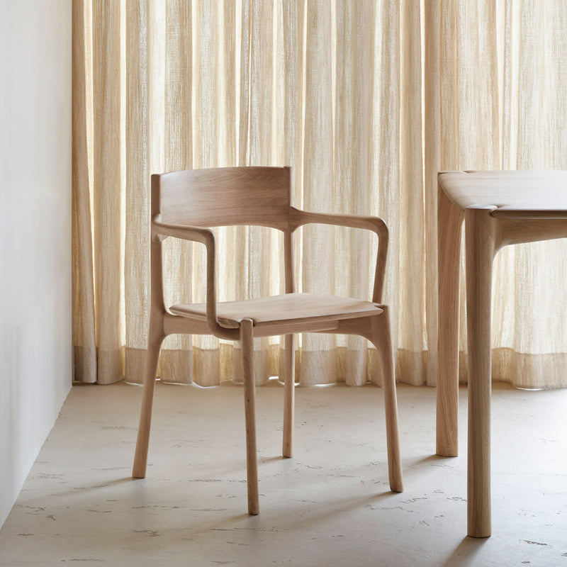 Pi oak dining chair next to a pi dining table in front of beige curtains.