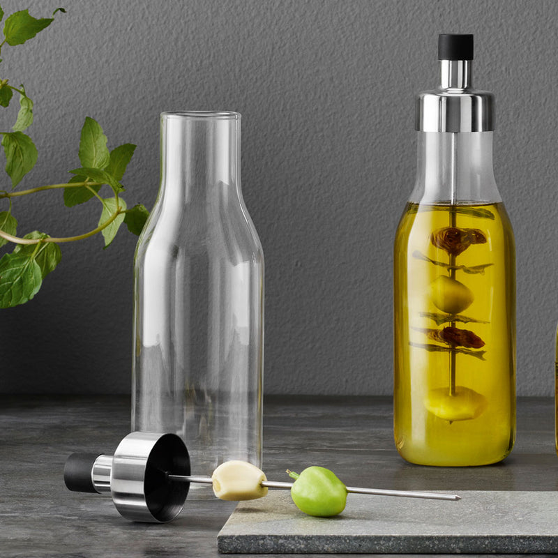 glassbottle with pouring lid ofr oils and dressings, shown open with garlic and olives on the stake ready to flavour oil