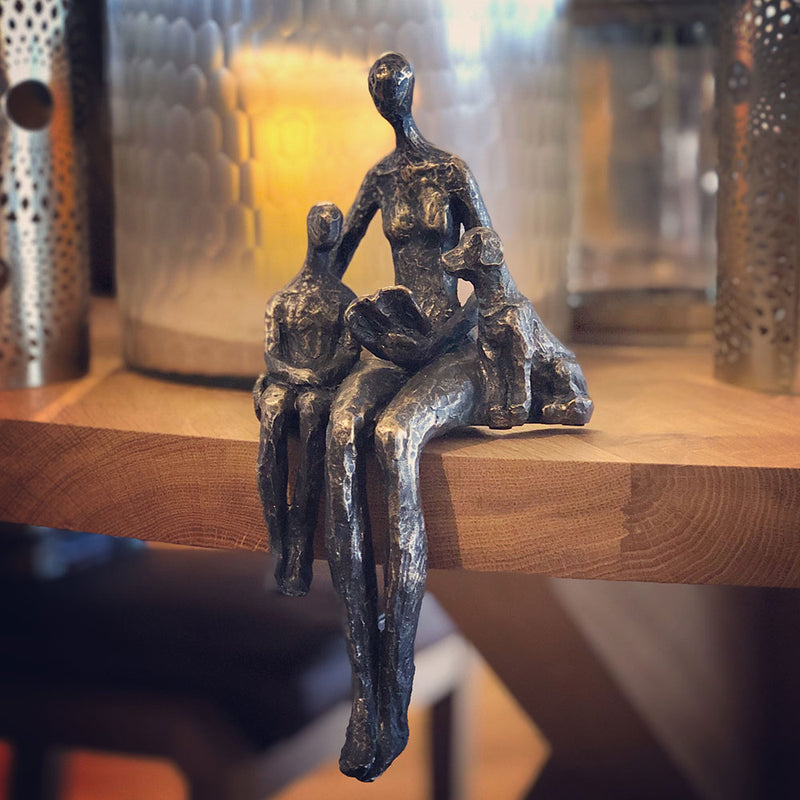 bronze seated sculpture of mother dog and child reading from a book, legs dangling over edge of shelf