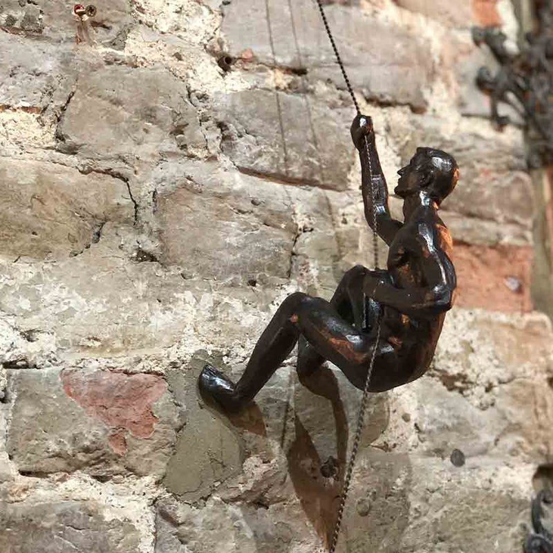 bronze climber on wire, hanging from the brick wall