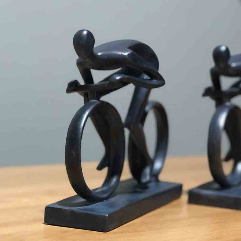cyclist sculpture is dark grey, both cyclust and bike are smooth in a henry moore style.