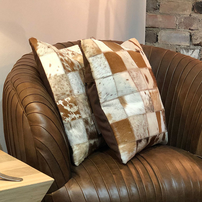 Cowhide cushion shown on brown leather chair.