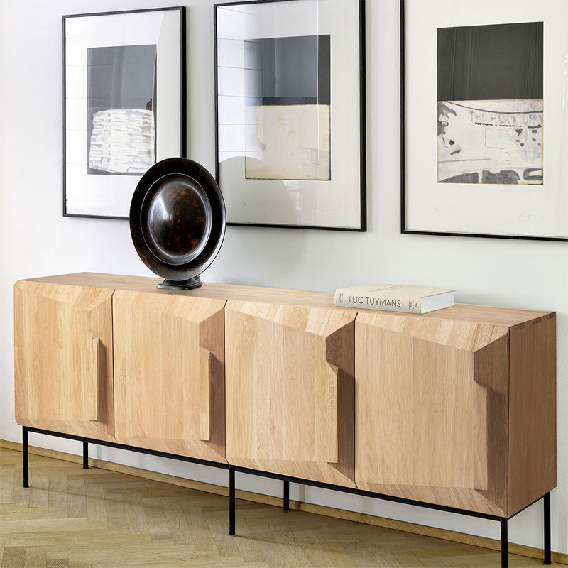 4 door sideboard with three pictures above. disc sculpture and book sit on top of sideboard