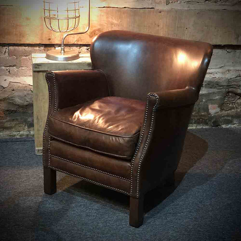 Studded arms and front on a classic chocolate brown leather armchair. leather side of the seat pad showing.