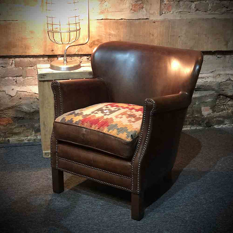 Studded arms and front on a classic chocolate brown leather armchair. Woven Kelim fabric seat.